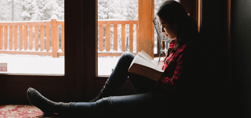 Mujer sentada frente a una ventana leyendo