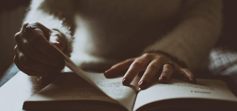 Libro abierto sujetado por las manos de una mujer que están pasando de página